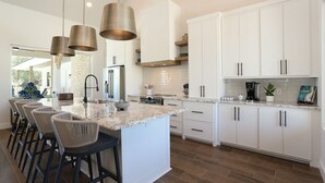 A modern kitchen with white cabinets, a large island with bar stools, stainless steel appliances, and pendant lighting.