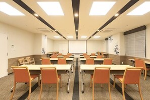 Ein Konferenzraum mit mehreren Tischen und Stühlen, einer Projektionsleinwand und einem großen Fenster mit Jalousien.