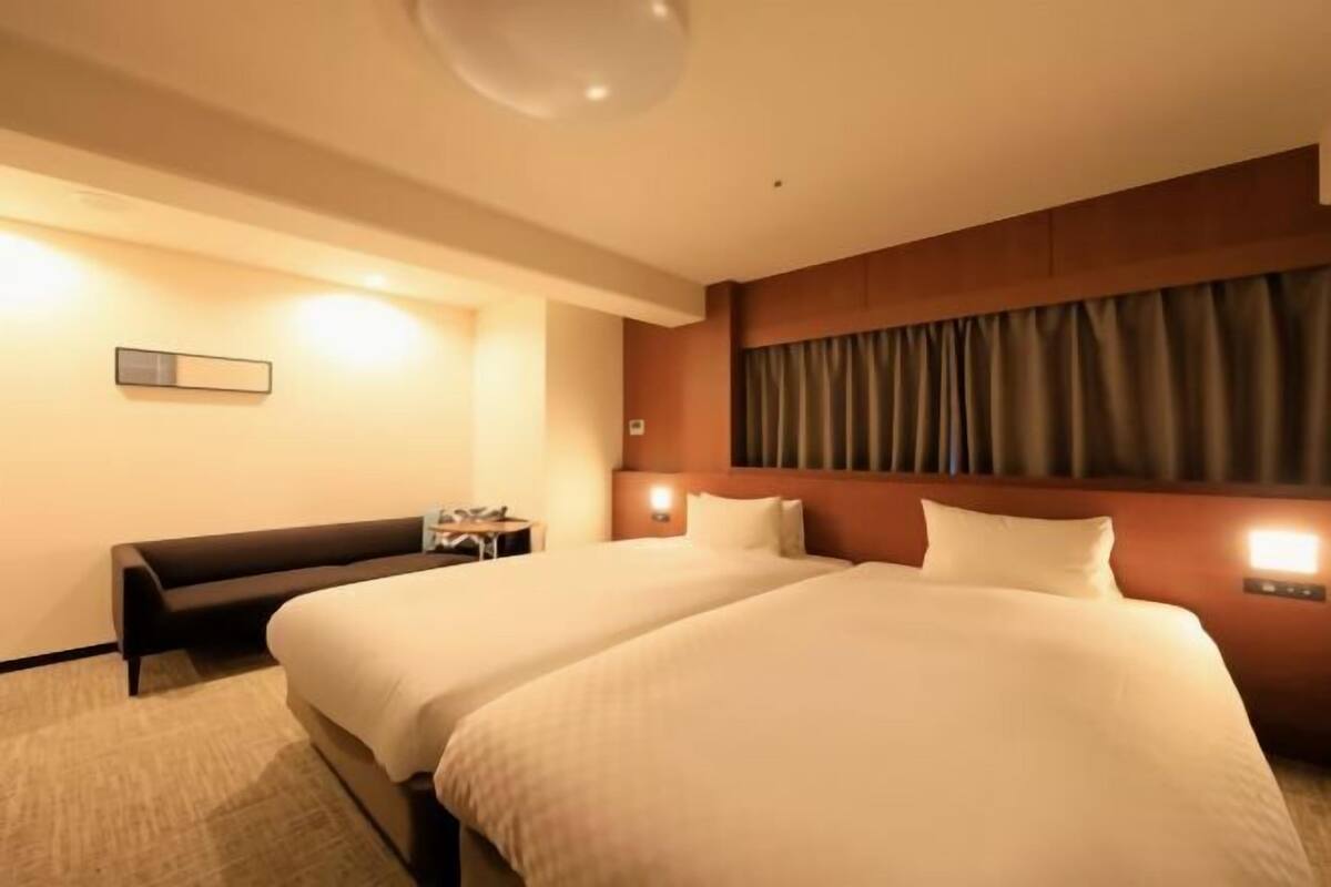 Een hotelkamer met twee bedden, een nachtkastje, een lamp en een wandlamp.