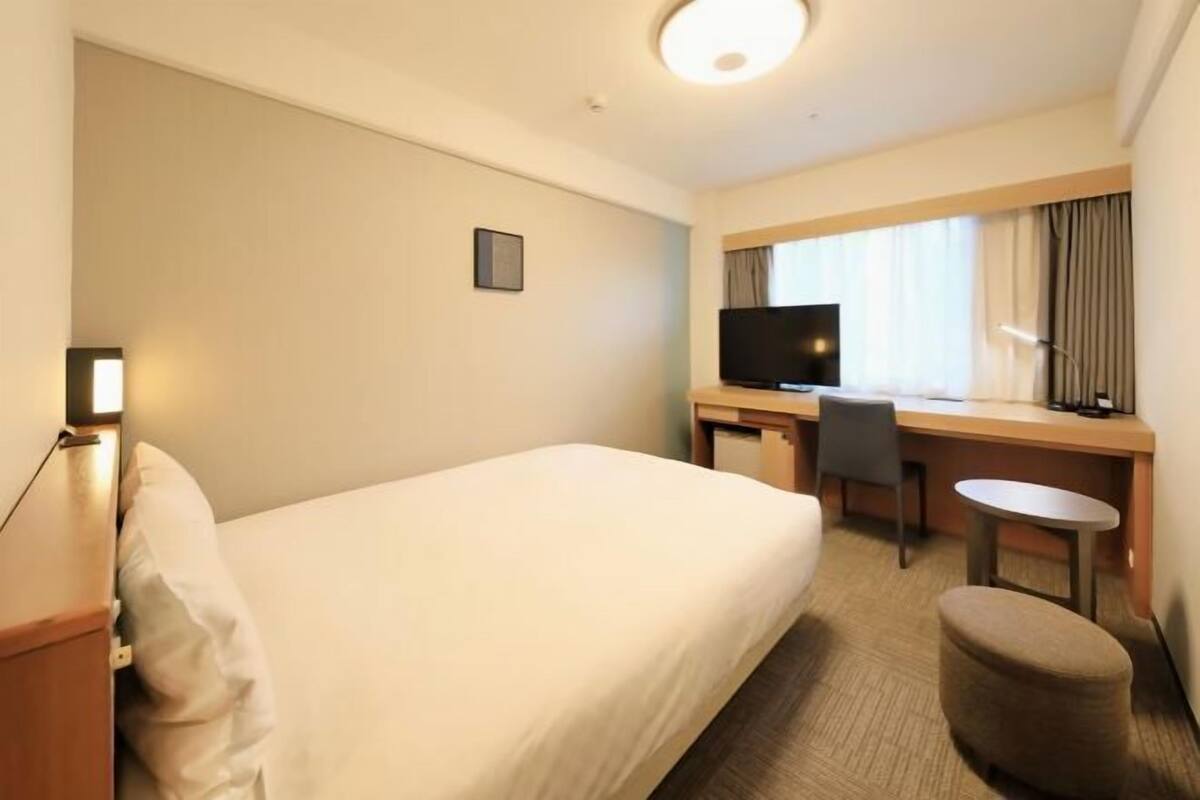Een hotelkamer met een bed, een bureau met stoel, een televisie en een kleine tafel.