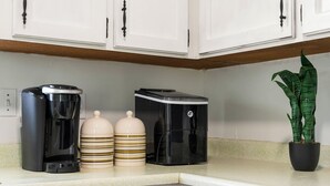 Una cucina con mobili bianchi, una macchina da caffè, due contenitori a righe e una pianta in vaso.