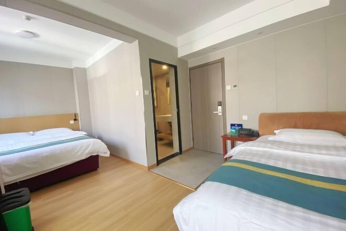 Habitación de hotel con dos camas, piso de madera, un bote de basura verde y una puerta que da a otra habitación.
