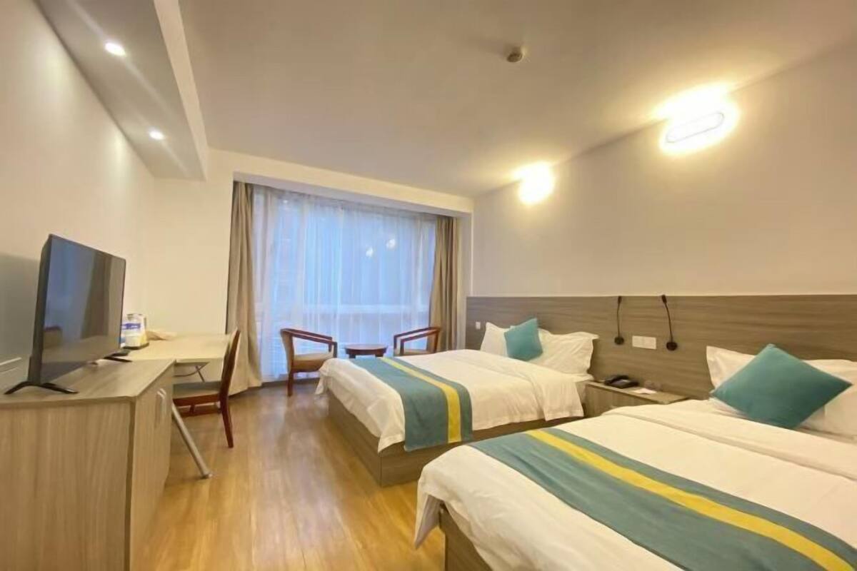 Habitación de hotel con dos camas, un escritorio con ordenador, una silla y un ventanal con cortinas.