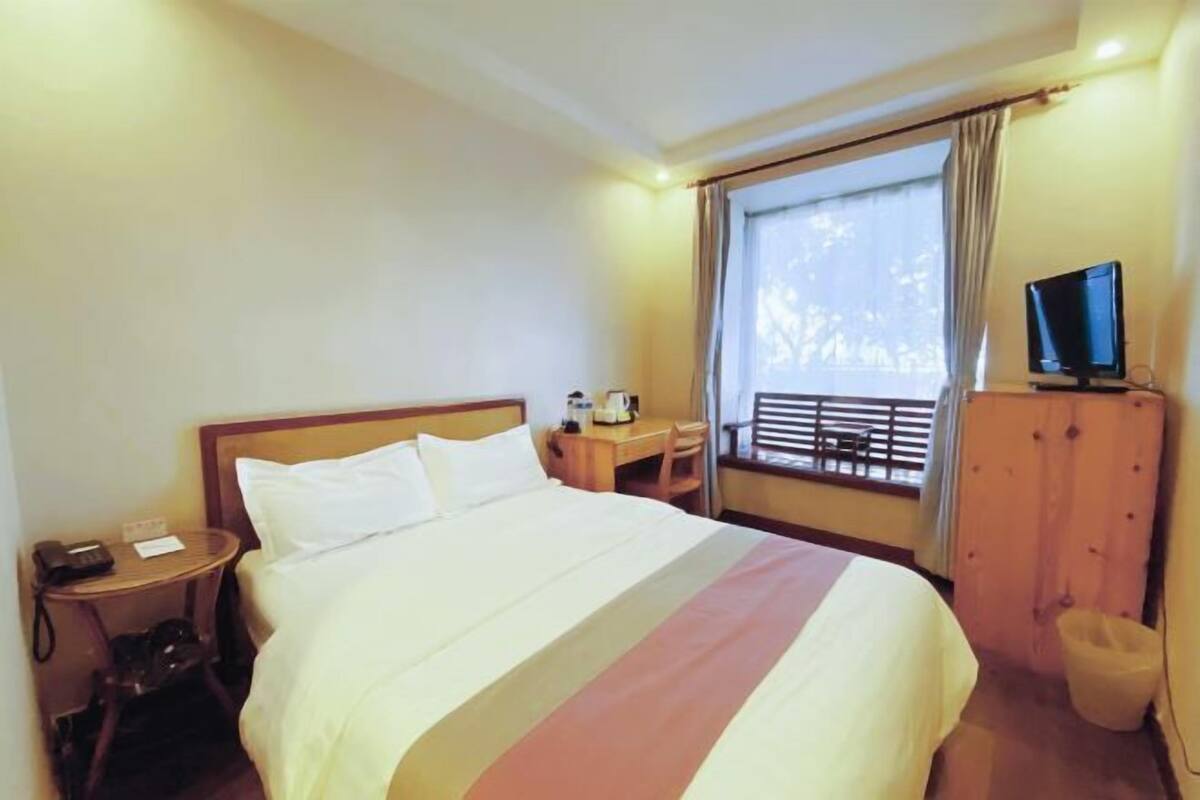 Una habitación de hotel con cama, escritorio, silla, televisor y ventana con cortinas.
