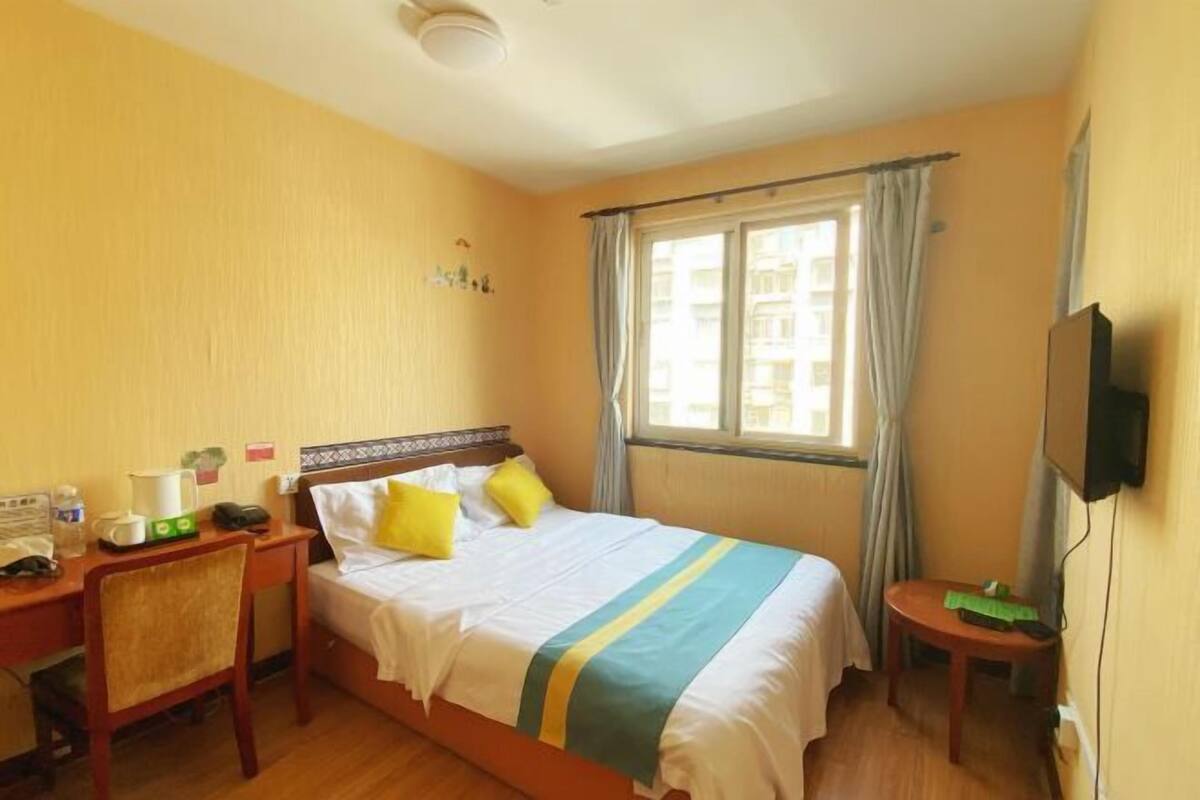 Habitación de hotel con cama, escritorio, silla, televisor y ventana con cortinas.
