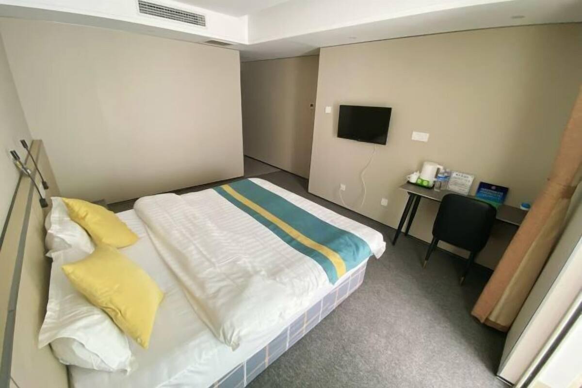Habitación de hotel con cama, escritorio, silla, televisor y una mesita de noche con artículos de aseo.