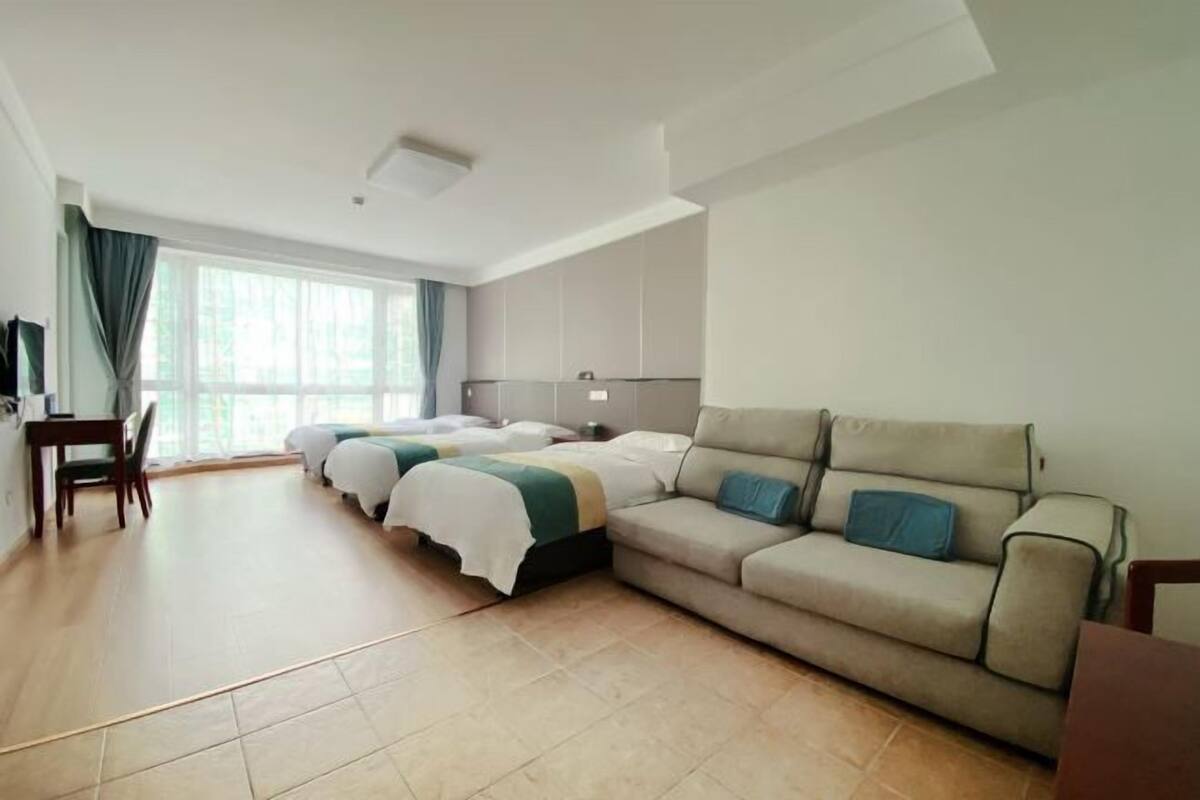Habitación de hotel con una cama grande, un sofá, un escritorio y un ventanal con cortinas.