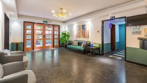 Een ruime lobby met een receptiebalie, een zithoek en een grote plant.