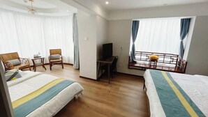 Hotelkamer met twee bedden, een bureau, een televisie en een balkon met gordijnen.