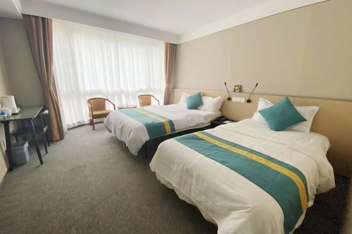 Habitación de hotel con dos camas, un escritorio, una silla y un ventanal con cortinas.