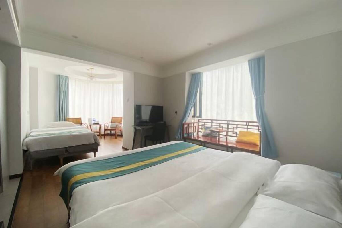 Habitación de hotel con dos camas, televisor, escritorio y balcón con cortinas.