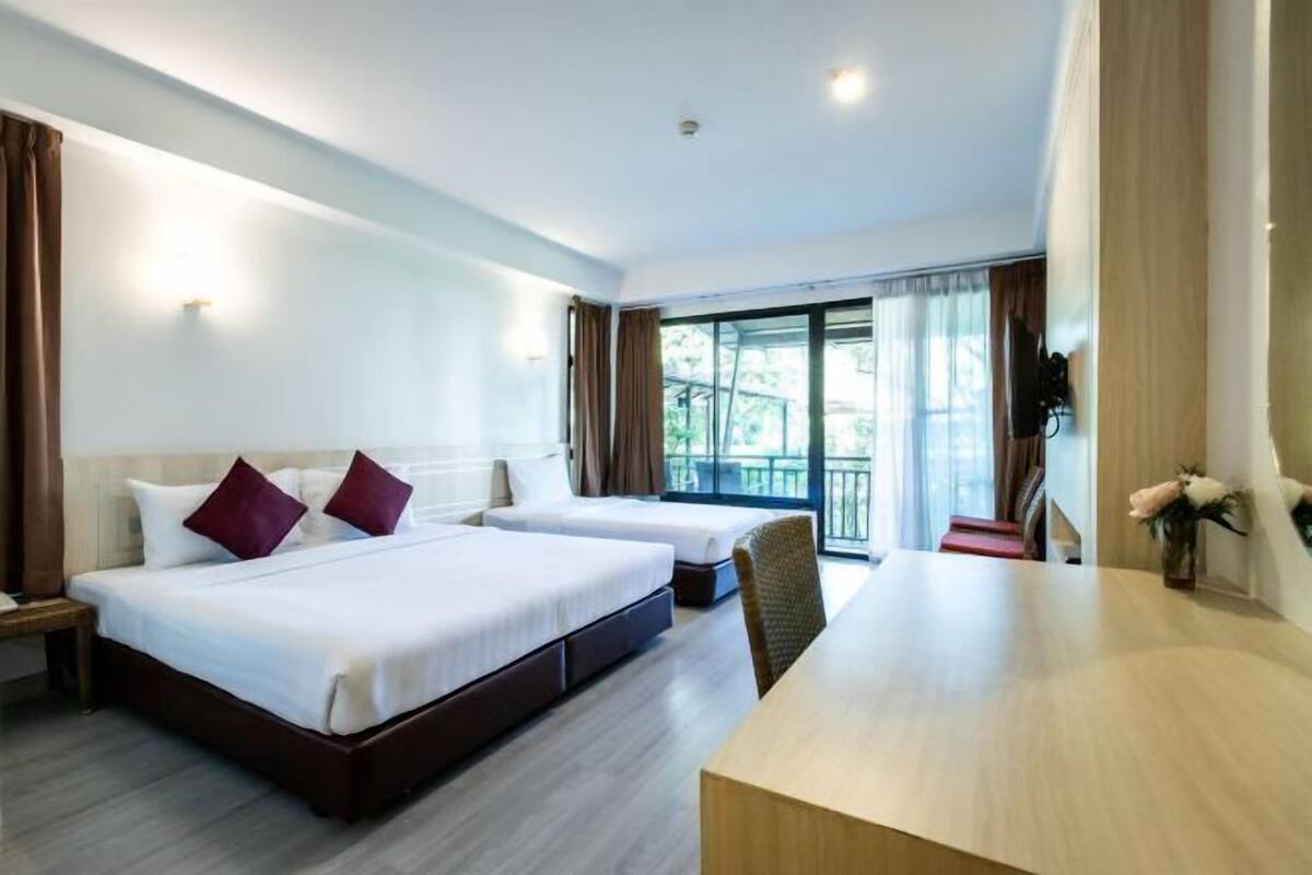 A hotel room with two beds, a desk, and a balcony with curtains.