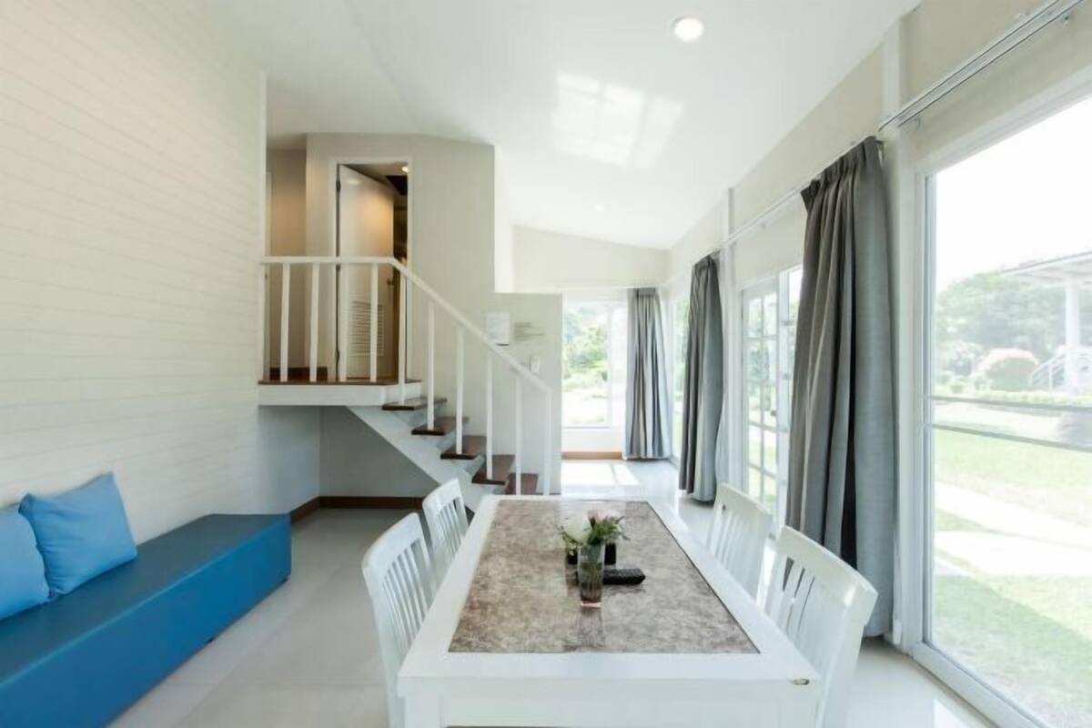 A modern interior with a dining table, white chairs, a blue bench, and a staircase leading to an upper level.