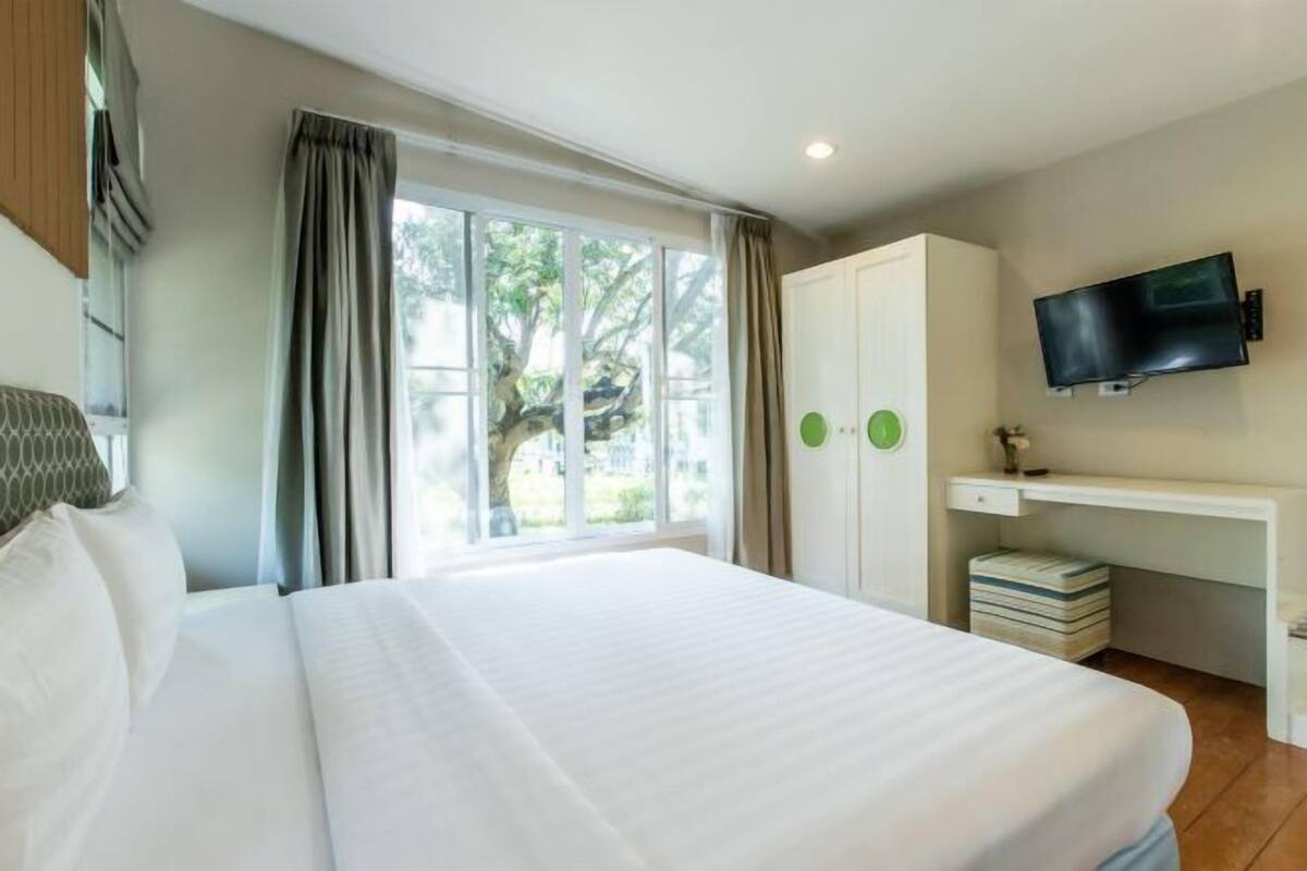A hotel room with a large bed, a desk with a TV, and a window with curtains.
