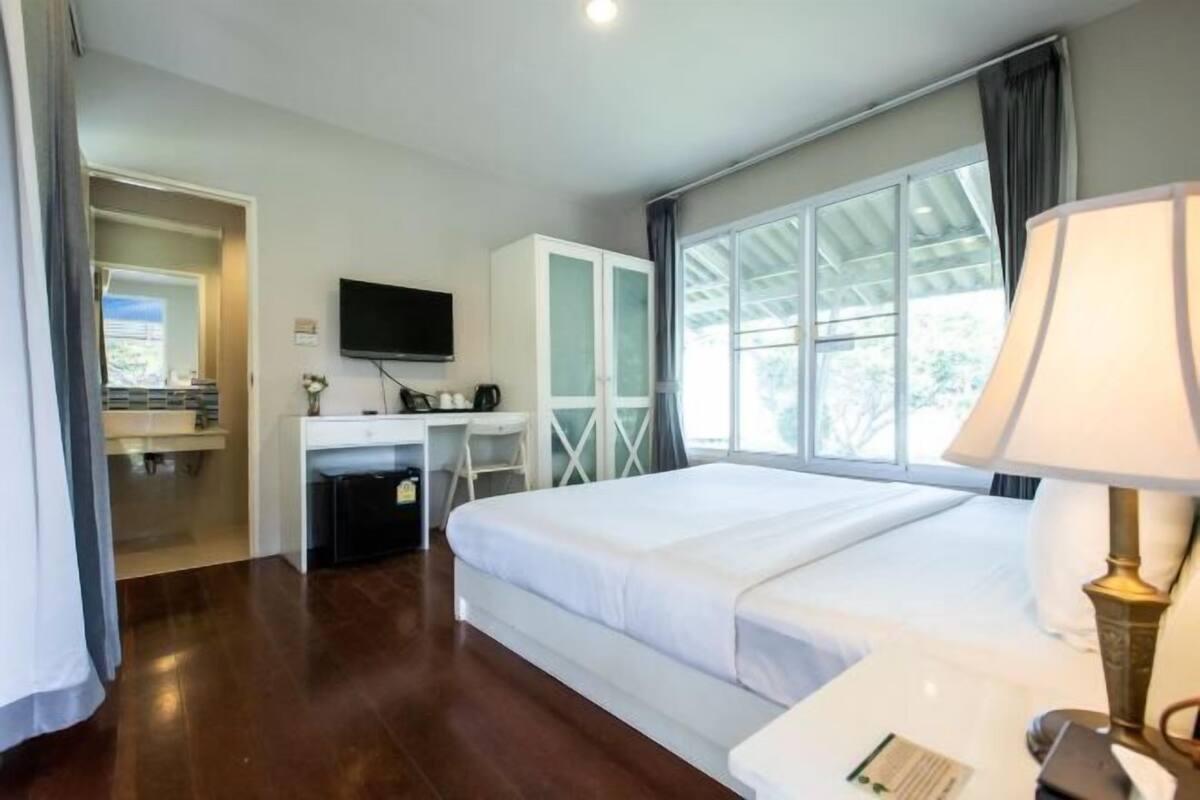 A hotel room with a bed, desk, TV, wardrobe, and large windows.