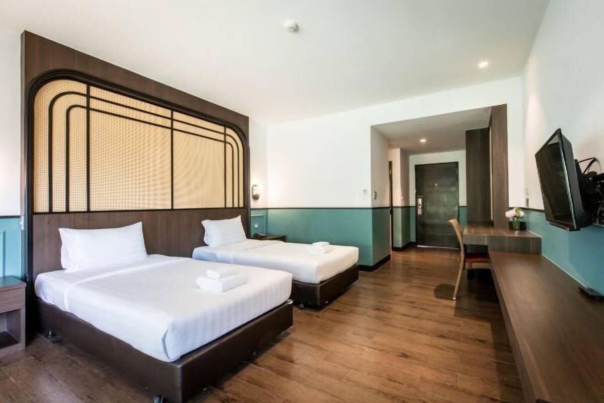 A hotel room with two beds, a wooden floor, a TV, and a desk.