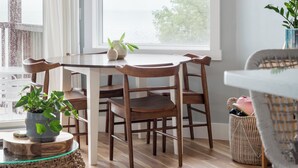 Un coin repas avec une table ronde, des chaises en bois et une vue dégagée sur l’extérieur grâce à une grande fenêtre.