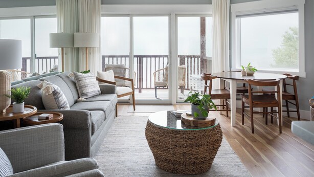 Un vaste espace de vie comprenant un canapé, des fauteuils, une table basse en verre et un balcon avec un ensemble de mobilier de jardin.