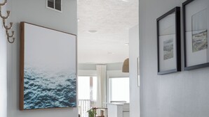 Un couloir orné d’un grand tableau encadré représentant l’océan, d’une plante en pot et, au fond, d’une chaise en osier.