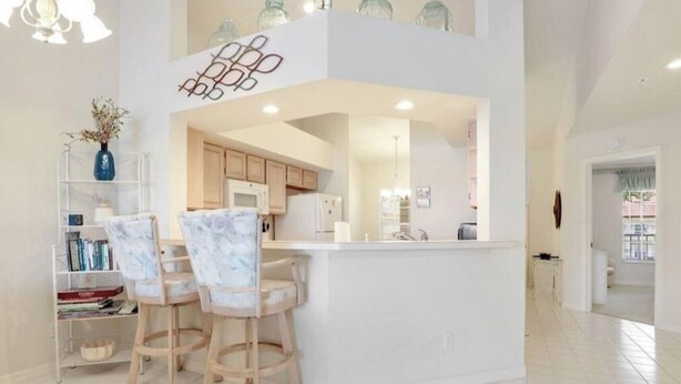 A modern kitchen with a central island, white cabinetry, and a dining area with bar stools. - " SPANISH WELLS GOLF & CC "     Chilled Pool for summer fun! (Bonita Springs)