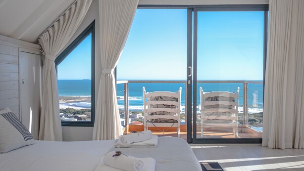 Ein Hotelzimmer mit einem großen Bett, einem Balkon mit Sitzgelegenheiten und Meerblick.