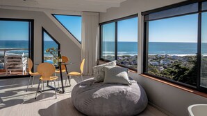 Ein modernes Schlafzimmer mit großen Fenstern, einem runden Sitzsack und Blick aufs Meer.