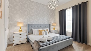 Une chambre moderne avec un grand lit, deux tables de chevet avec des lampes, un mur orné d’un motif géométrique et une fenêtre avec des rideaux foncés.