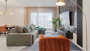 Un salon moderne comprenant un canapé, une table basse, un téléviseur fixé au mur et un coin repas avec une table et des chaises.