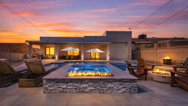 A modern outdoor pool area with a fire feature, lounge chairs, and umbrellas.