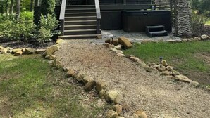 Een chalet met een overdekte veranda, een trap die erheen leidt, en een omliggend bebost gebied.