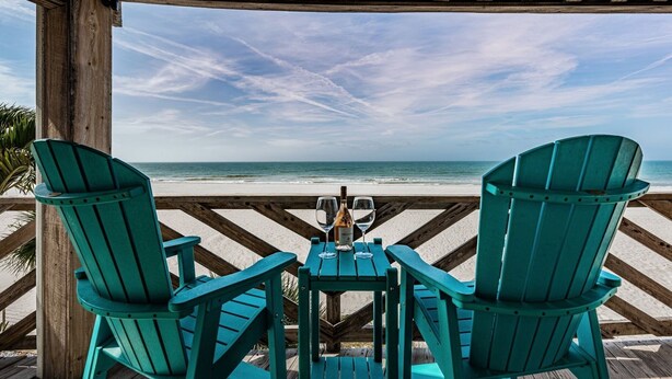 Una terraza de madera con dos sillas Adirondack verdes mirando a la playa.