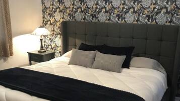Una cama con cabecera capitonada, una mesita de noche con lámpara y papel tapiz estampado.