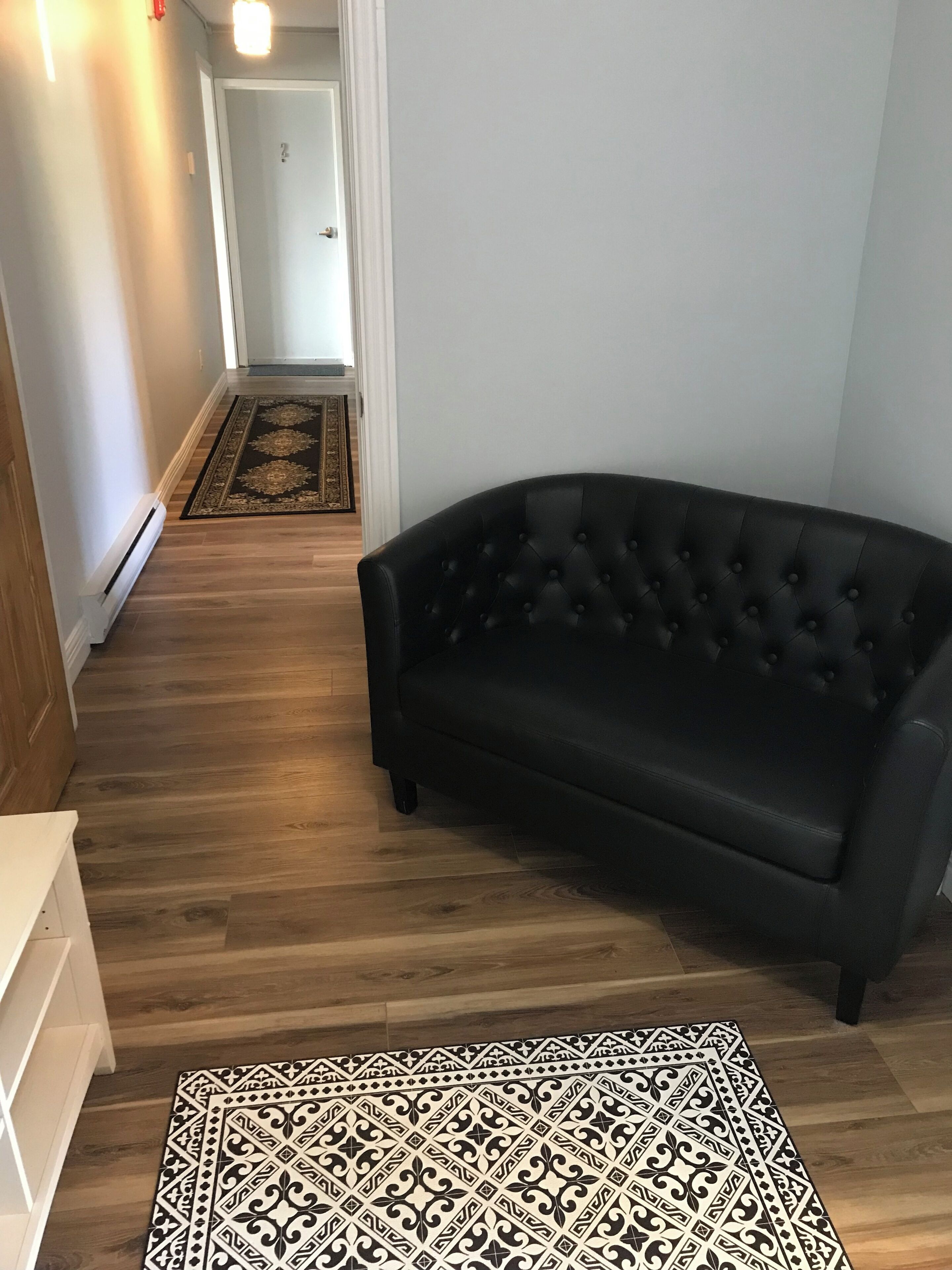 A hallway with a black leather sofa, a patterned rug, and a wooden floor.