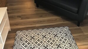 Un pasillo con un sofá de cuero negro, un tapiz estampado y piso de madera.