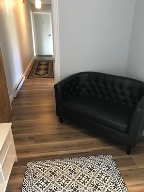 Un pasillo con un sofá de cuero negro, un tapiz estampado y piso de madera.
