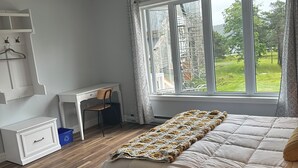 Un dormitorio con una cama grande, un escritorio y una silla. Hay una ventana con vista a la vegetación.