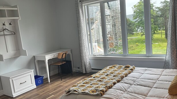 Un dormitorio con una cama grande, un escritorio y una silla. Hay una ventana con vista a la vegetación.