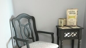Una silla de madera oscura con asiento y respaldo acolchados, ubicada al lado de una pequeña mesa auxiliar de madera con una placa y un cuadro enmarcado.