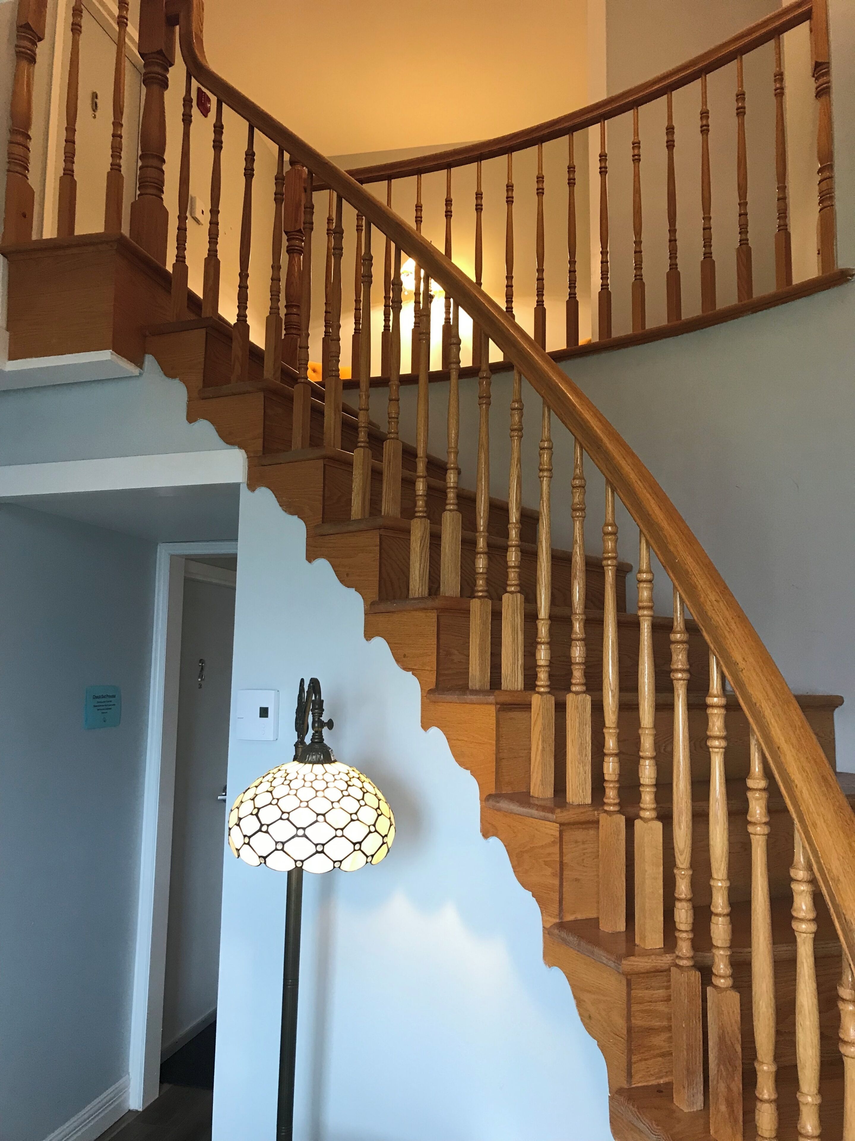 A wooden staircase with a unique curved design and a wall-mounted lamp.