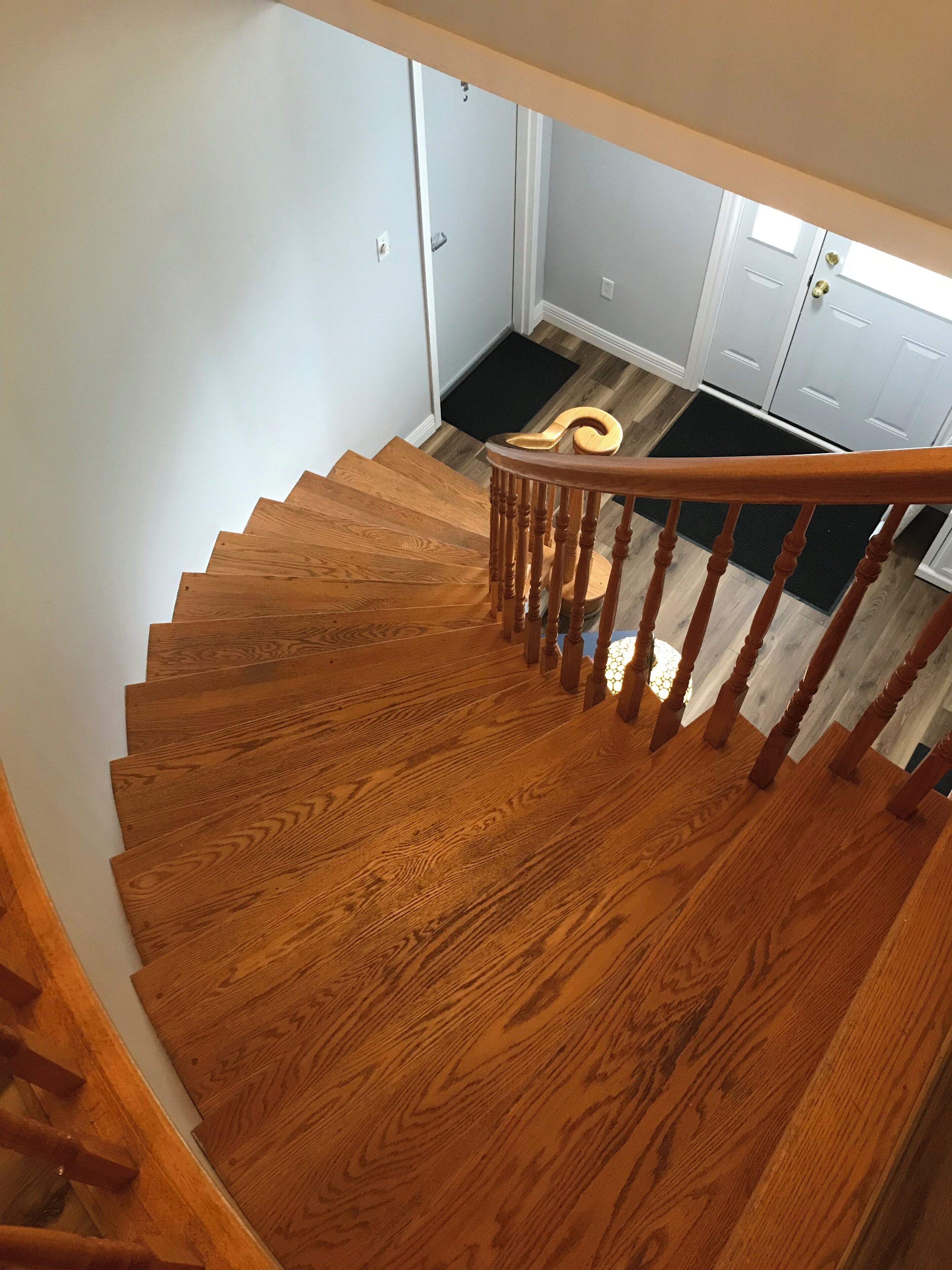 Un escalier en bois menant à un palier où se trouvent un paillasson noir et une porte blanche.