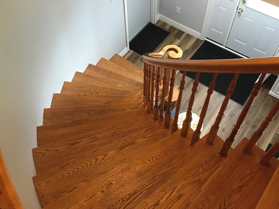 Una escalera de madera que lleva a un rellano con un felpudo negro y una puerta blanca.