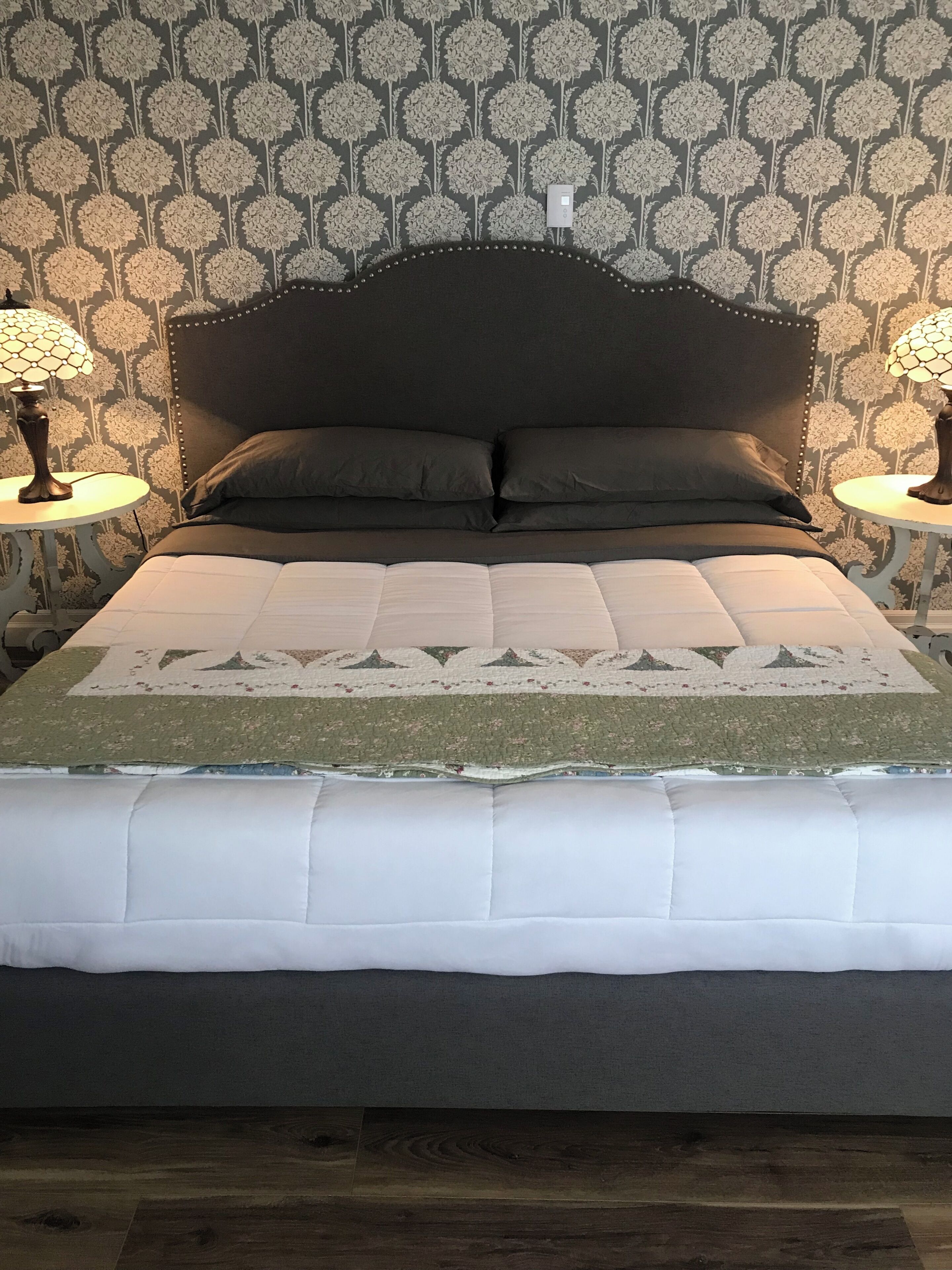A bed with a dark headboard, two bedside lamps, and a patterned wall.