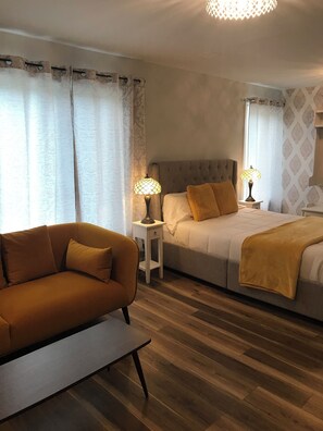 Une chambre à coucher avec un lit, une table de chevet avec une lampe, un canapé et un plancher en bois.