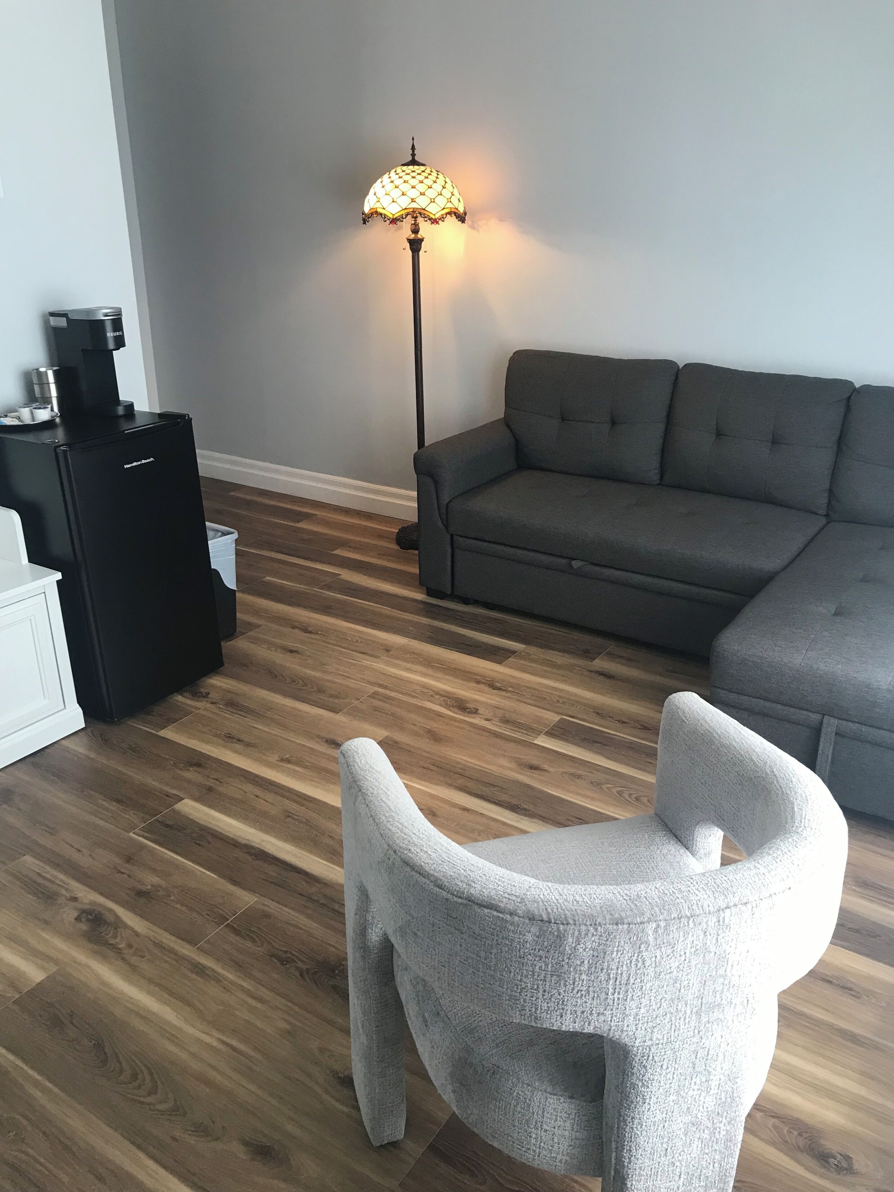 A modern living room with a grey sofa, a white armchair, and a coffee machine.