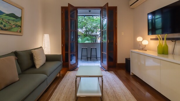 A modern living room with a sofa, a coffee table, and a kitchen area with a TV and bar stools.