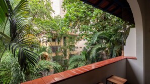 A balcony with two wooden chairs and a red-tiled ledge overlooking a lush garden with various plants and a building in the background.