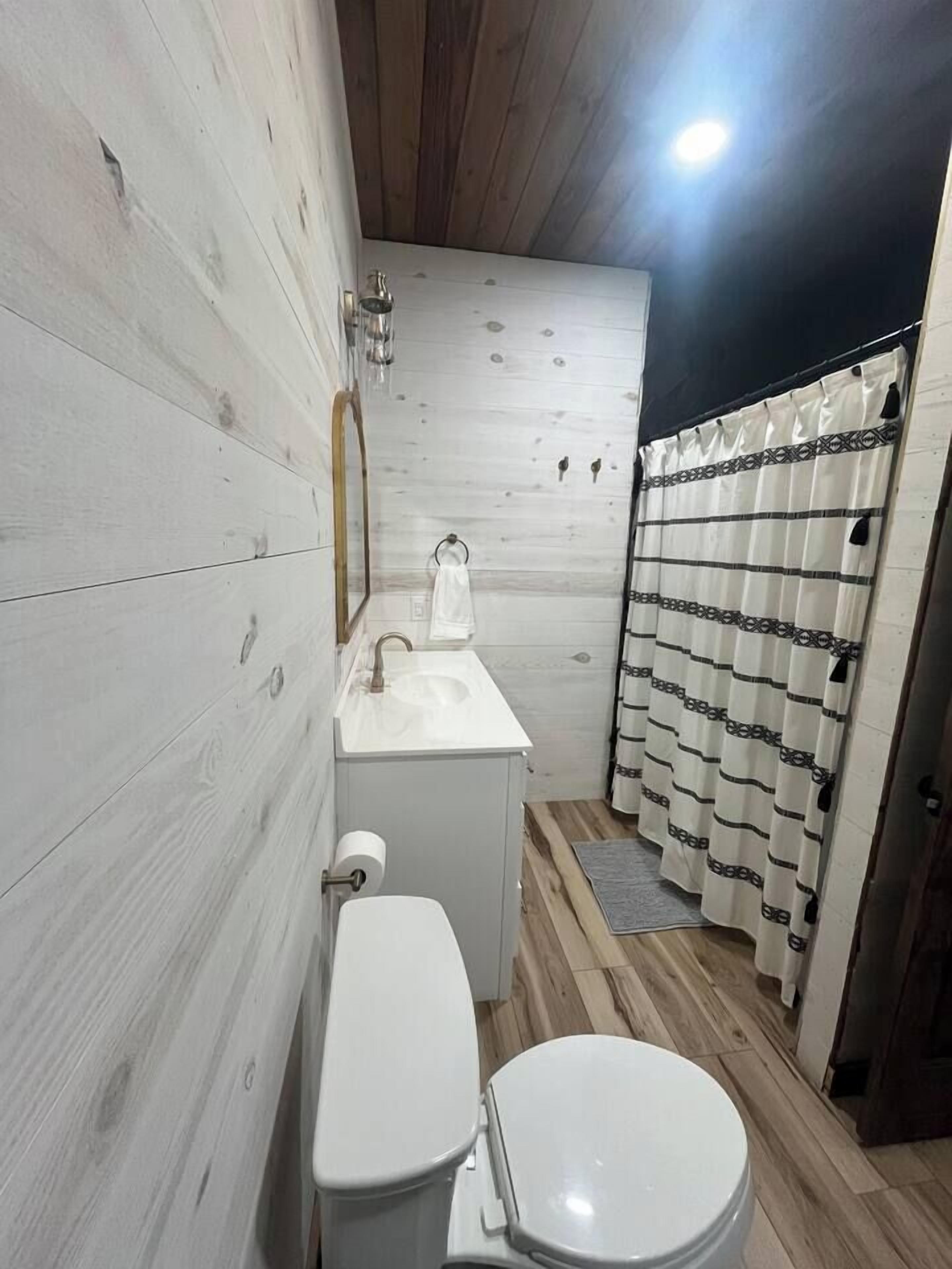 Et lille badeværelse med toilet, vask og bruseforhæng.