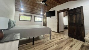Une chambre à coucher avec un lit, un bureau, une chaise, un téléviseur fixé au mur et un plafond en bois.