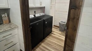 Une cuisine de taille réduite avec des meubles blancs, un réfrigérateur noir et un plancher en bois.