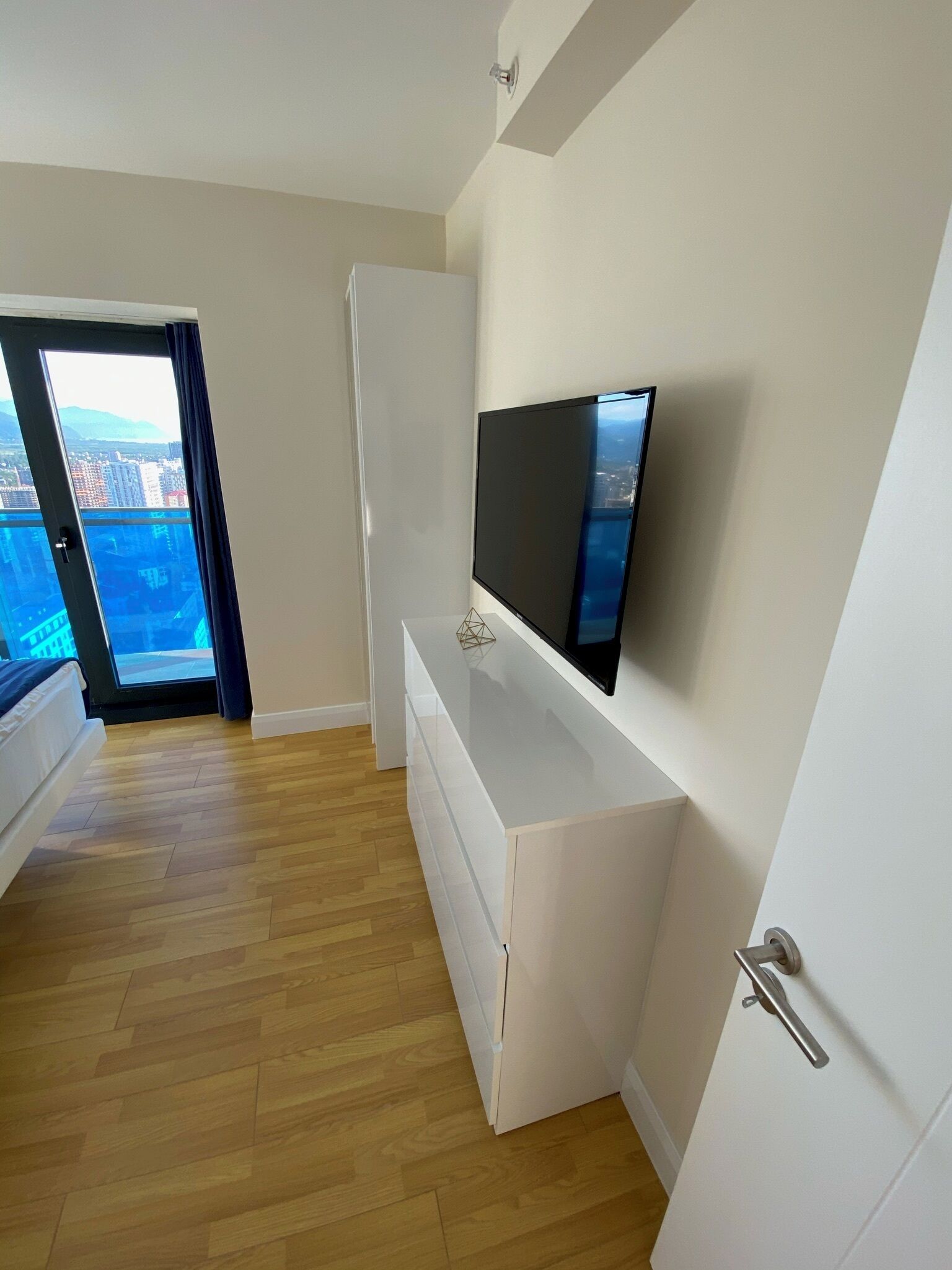 Una habitación moderna y minimalista con un ventanal grande, un televisor de pantalla plana montado en la pared y piso de madera.